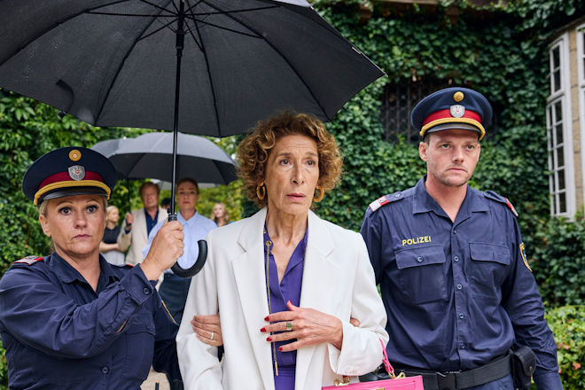 Komödie "Mama ist die Best(i)e": Gloria Almeda (Adele Neuhauser, M.) wird von Polizisten (Komparsen) abgeführt. Sie wird verdächtigt, ihren Ehemann Victor umgebracht zu haben.